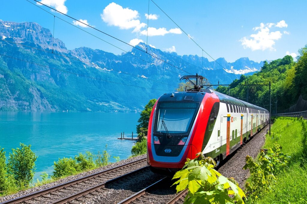 Modern Swiss train traveling through scenic alpine landscape with mountains and green meadows.