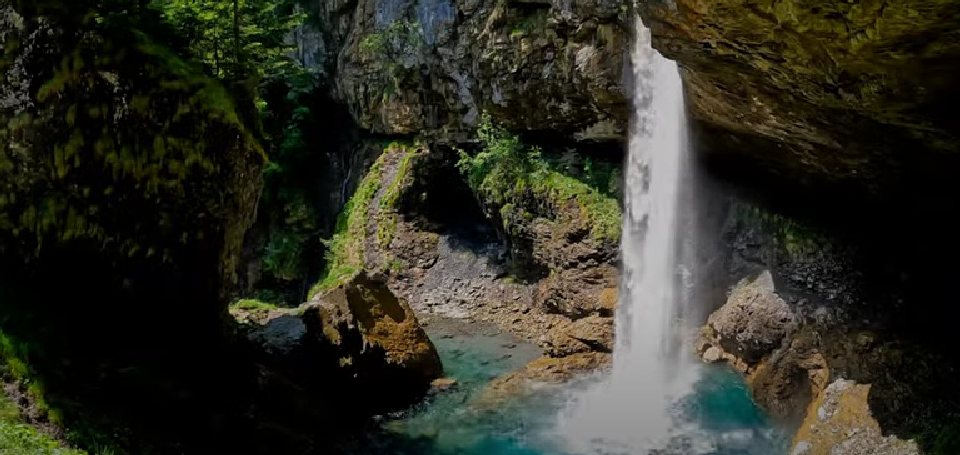 Berglistüber Wasserfall pouring behind a rocky overhang in the Glarus region, a captivating example of hidden waterfall wonders in Switzerland, framed by alpine forest and misty cliffs.