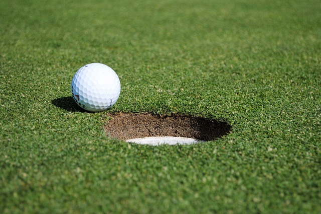 Close-up of a white golf ball about to drop into the hole on a green golf course.